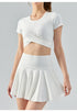 Woman wearing white tennis set with short-sleeve crop top and high-waist flared skirt.