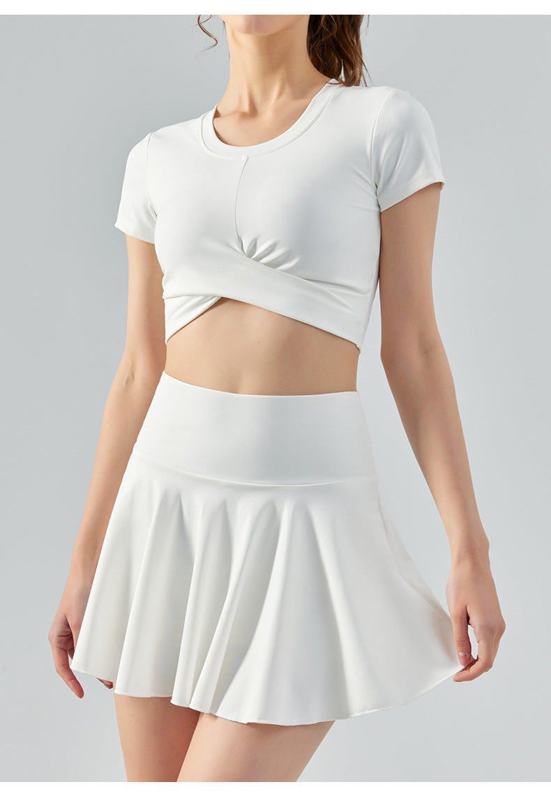Woman wearing white tennis set with short-sleeve crop top and high-waist flared skirt.