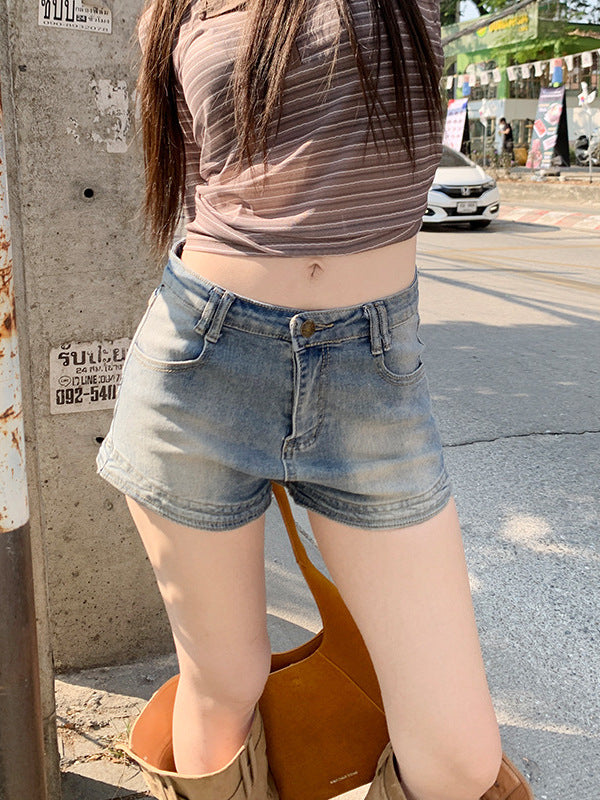 Woman standing outdoors in faded high waist denim shorts and carrying a tan handbag.