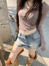 Woman in high waist faded denim shorts and brown striped crop top, posing on a sidewalk.