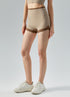 Model stands in khaki shorts with brown trim and white sneakers.