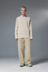Person wearing a khaki half zip long sleeve t shirt styled with beige pants on a gray background