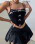 Woman wearing a black lace-trimmed corset with pink bows and thin straps, paired with a black draped mini skirt.