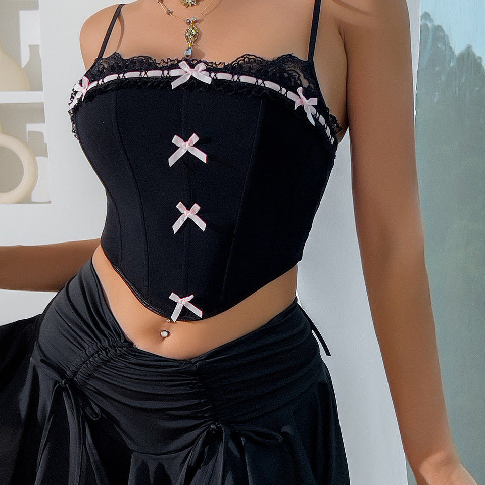 Close-up of a black corset with lace trim and pink bow accents, styled with layered necklaces and a black skirt.