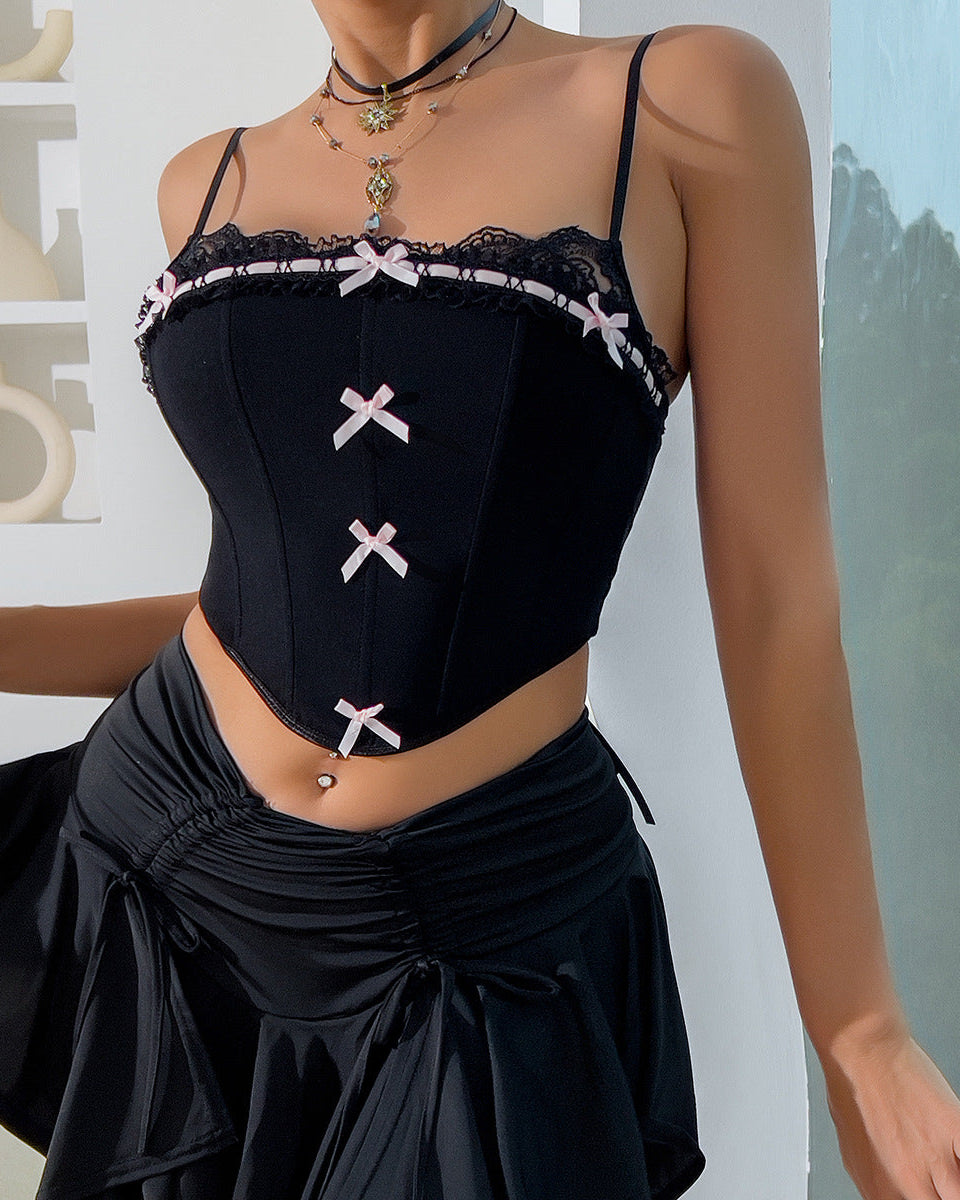 Close-up of a black corset with lace trim and pink bow accents, styled with layered necklaces and a black skirt.