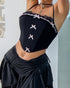 Woman lifting her arm slightly while showing a black corset top with lace and pink bow details and a ruched black skirt.