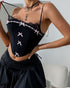 Woman holding a strap of her black corset top adorned with lace and pink bows, paired with a black mini skirt.