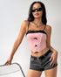 Woman posing in sunglasses, wearing a pink lace-trimmed corset top with black bows and black denim shorts.