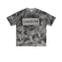 Flat lay of gray graphic tee with black “LIBERALISM” stencil text and abstract texture.