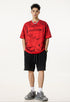 Model in red Liberalism tee and black shorts, standing front-facing with hands in pockets.