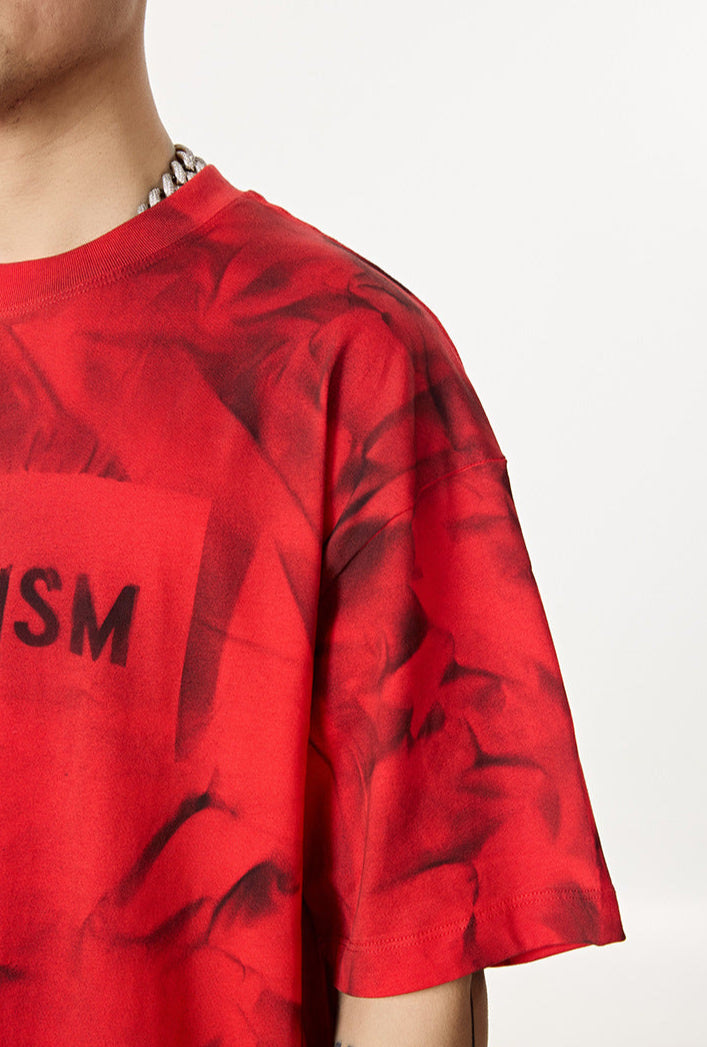 Close-up of red tee shoulder seam and sleeve with visible abstract pattern.