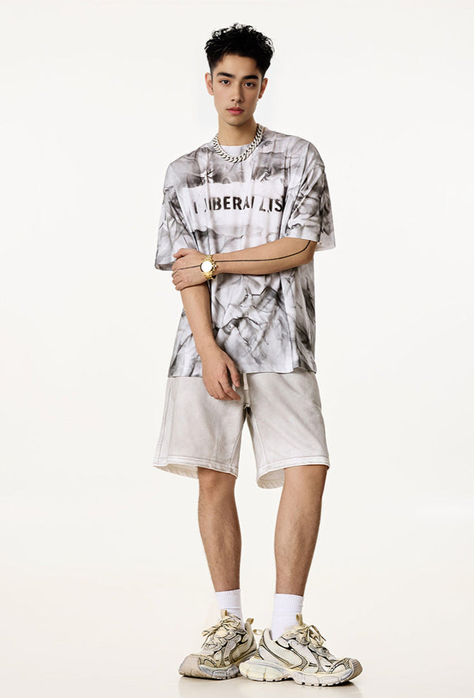 Man models white oversized graphic tee with “Liberalism” text and light shorts.