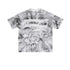 Flat lay of white graphic tee with black “LIBERALISM” stencil text and smoky crumple print.