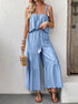 Woman holds wicker bag while wearing light blue cami and pants set.
