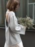 Person wearing a light gray backless sweater holding a bouquet of flowers indoors.