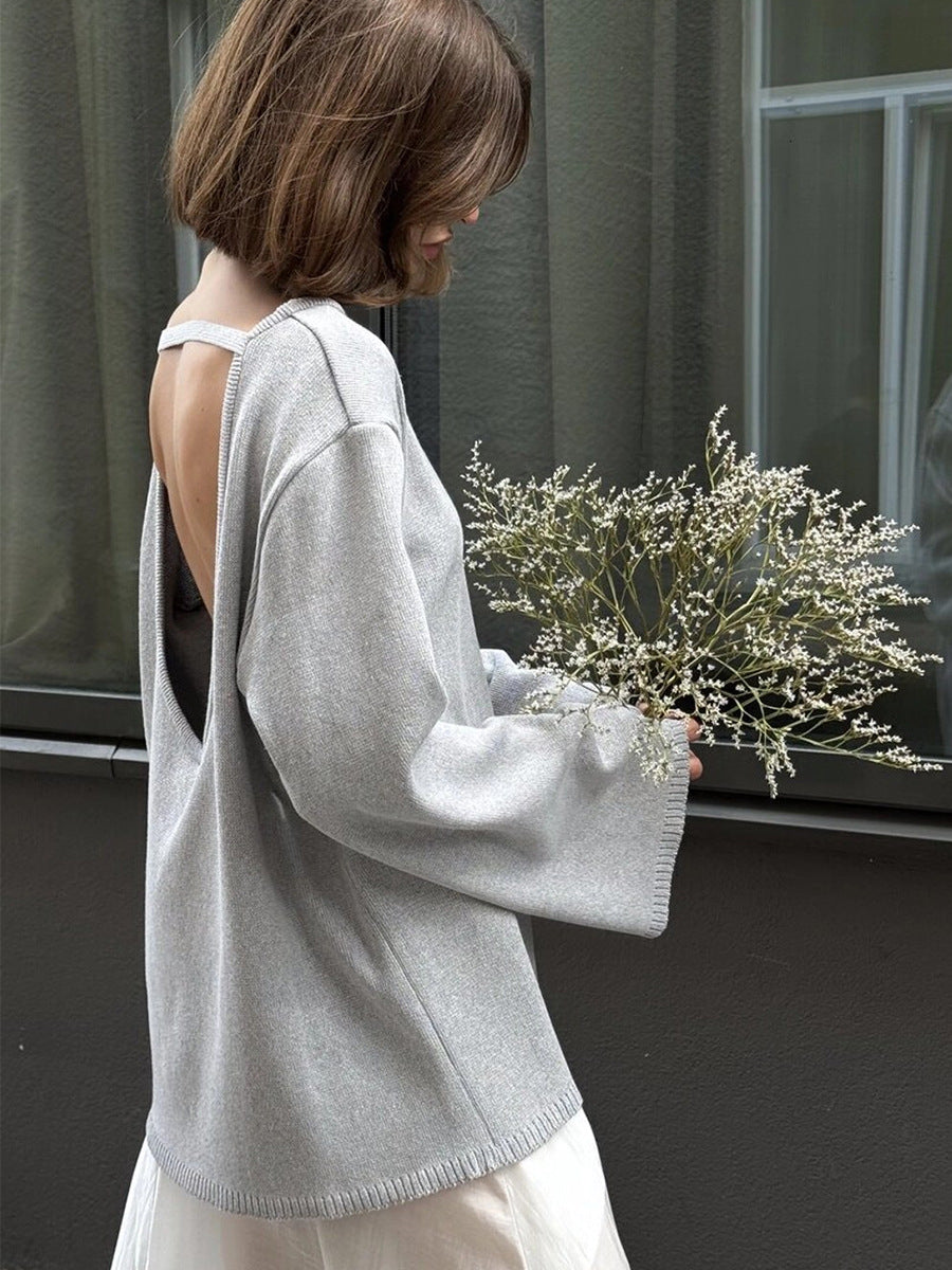 Person wearing a light gray backless sweater holding a bouquet of flowers indoors.