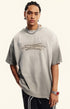 Man models light grey gradient quote tee against beige background with hands in pockets.