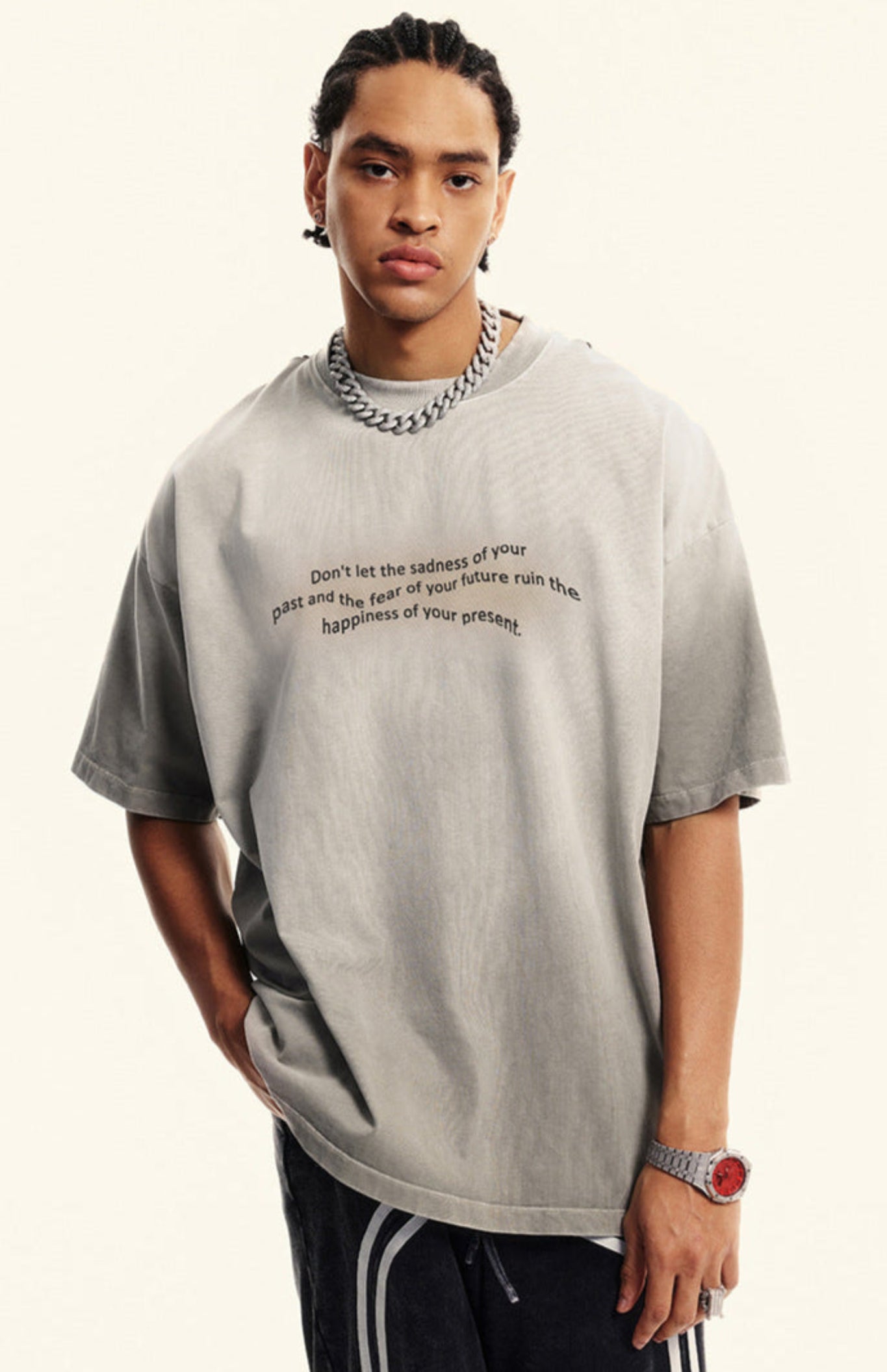 Man models light grey gradient quote tee against beige background with hands in pockets.