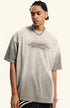 Man in light grey quote tee looks to side with relaxed pose, against plain background.
