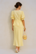 Woman wearing a yellow puff sleeve set holding a woven bag against a beige background