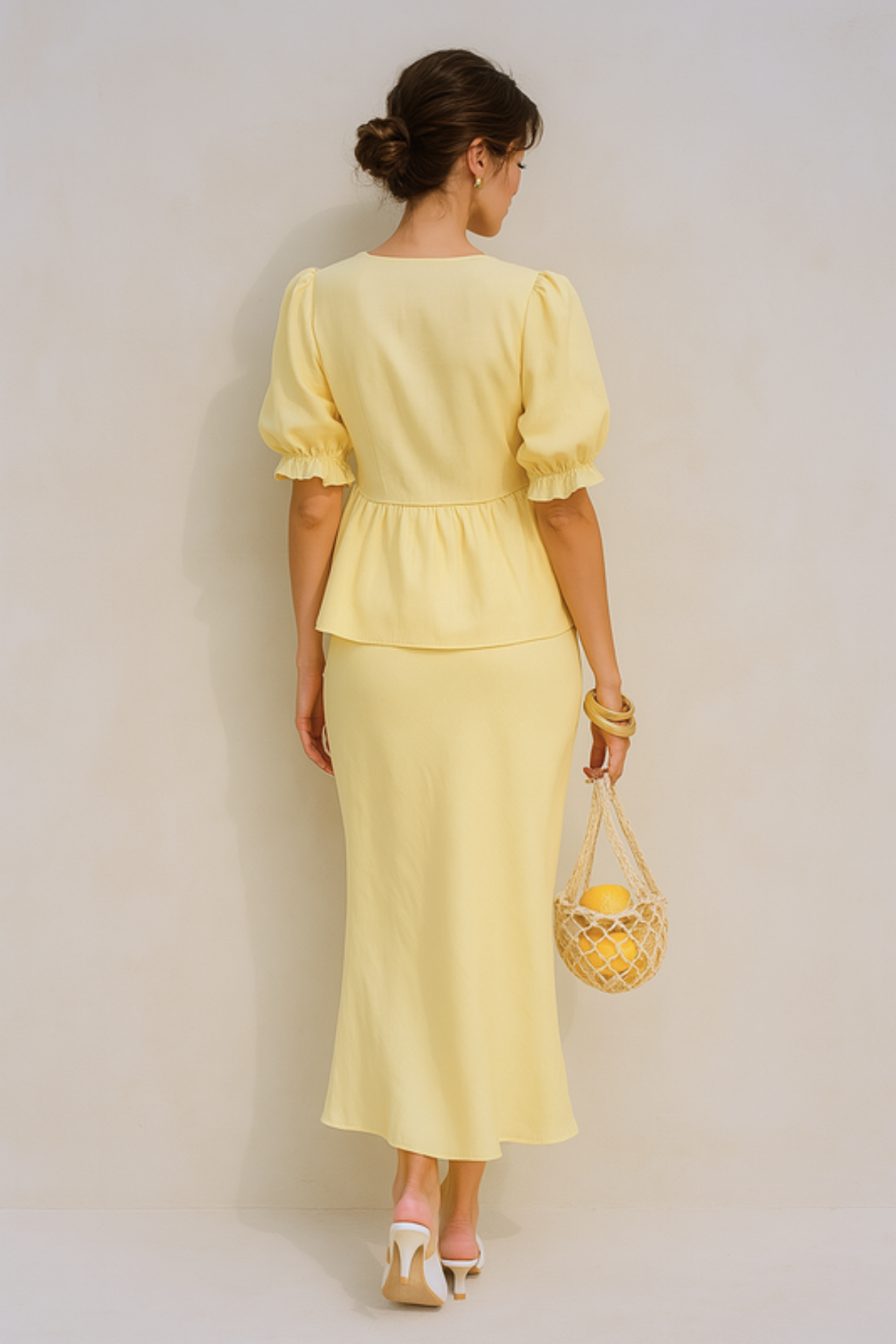 Woman wearing a yellow puff sleeve set holding a woven bag against a beige background
