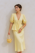 Woman wearing a yellow puff sleeve set holding a matching bag against a beige background