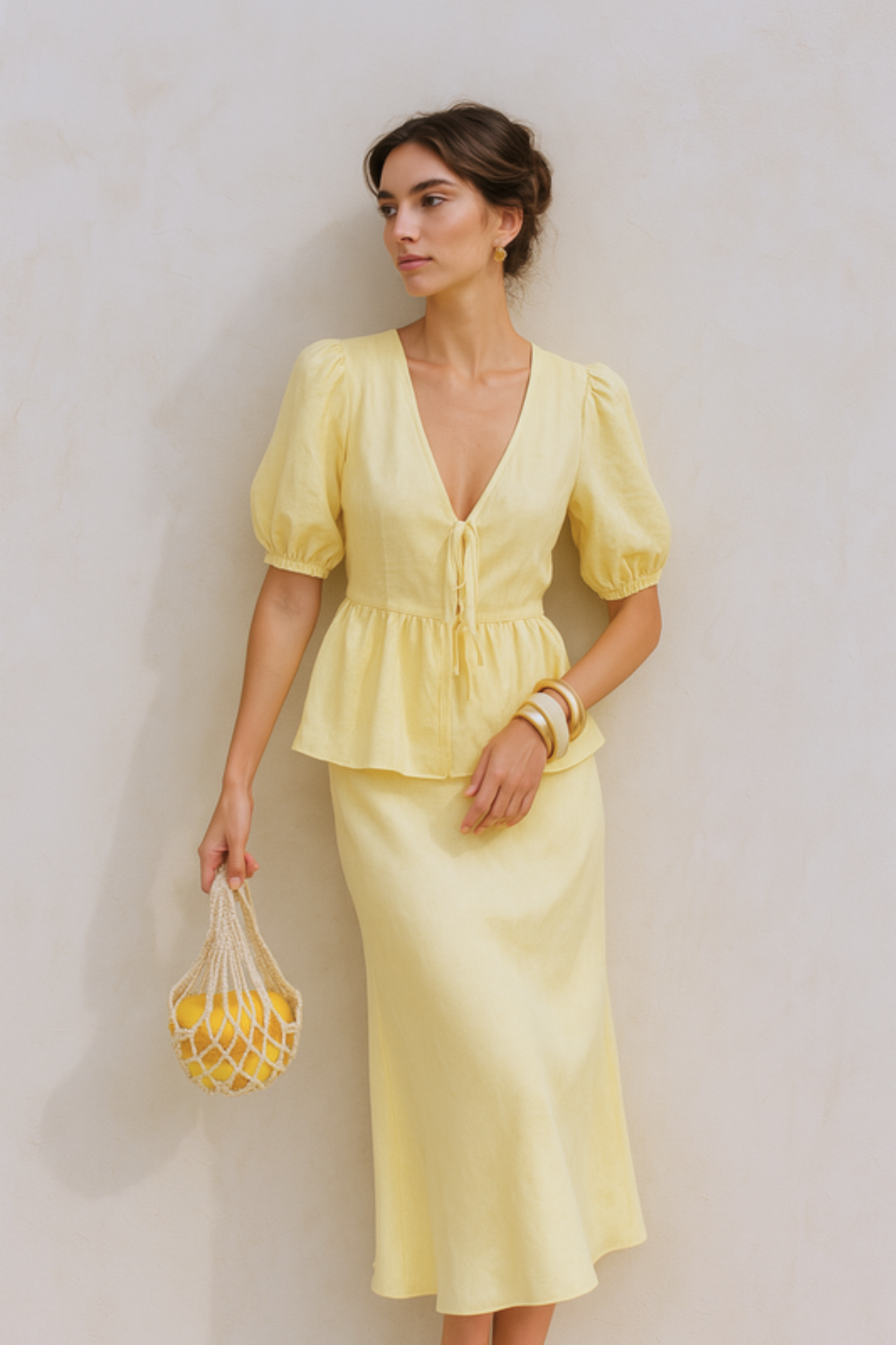 Woman wearing a yellow puff sleeve set holding a matching bag against a beige background