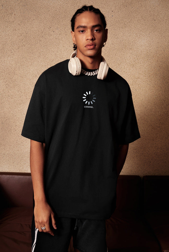 Man wearing black loading graphic tee with headphones around neck.