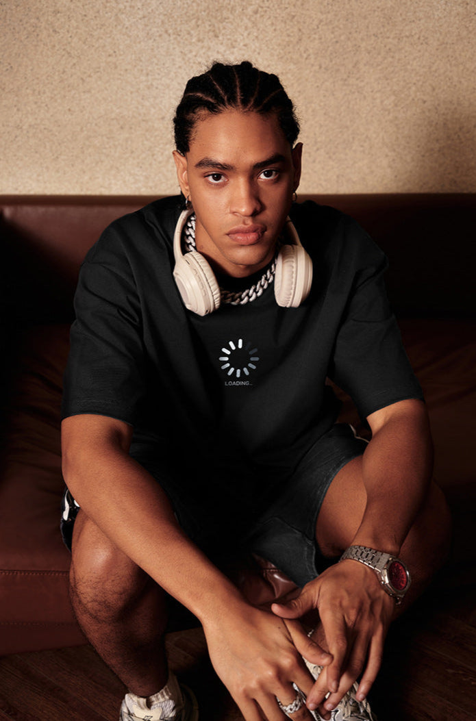 Man sitting on sofa wearing black loading tee and headphones.