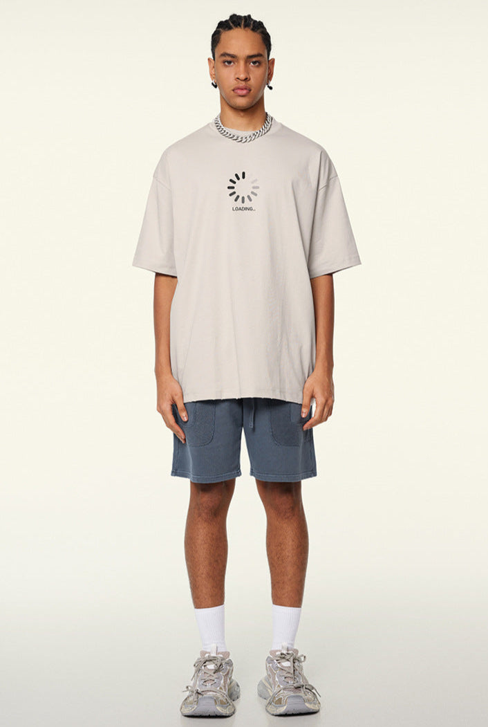 Man wearing cream loading tee with blue shorts and sneakers.