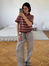 Model takes mirror selfie wearing brown striped polo shirt and wide-leg gray jeans.