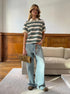 Model poses in cream and green striped polo shirt with wide-leg jeans and woven clutch.