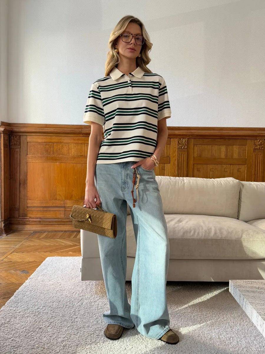 Model poses in cream and green striped polo shirt with wide-leg jeans and woven clutch.