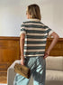 Back view of model in striped polo shirt and loose light-wash jeans, holding tan clutch.