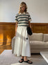 Model wears cream striped polo shirt tucked into white flowy skirt with black shoulder bag.