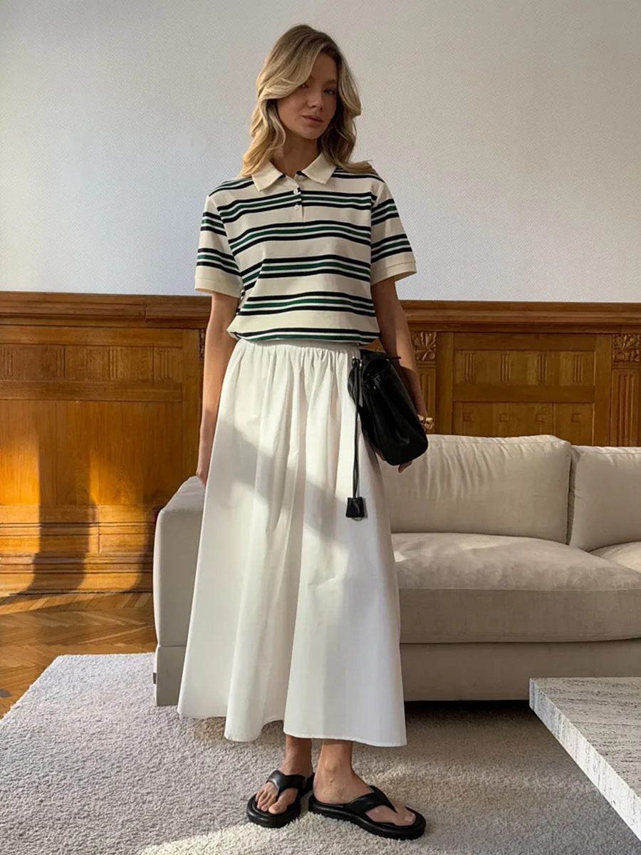 Model wears cream striped polo shirt tucked into white flowy skirt with black shoulder bag.