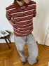 Model stands in brown striped polo shirt with hands behind back, wearing gray denim pants.
