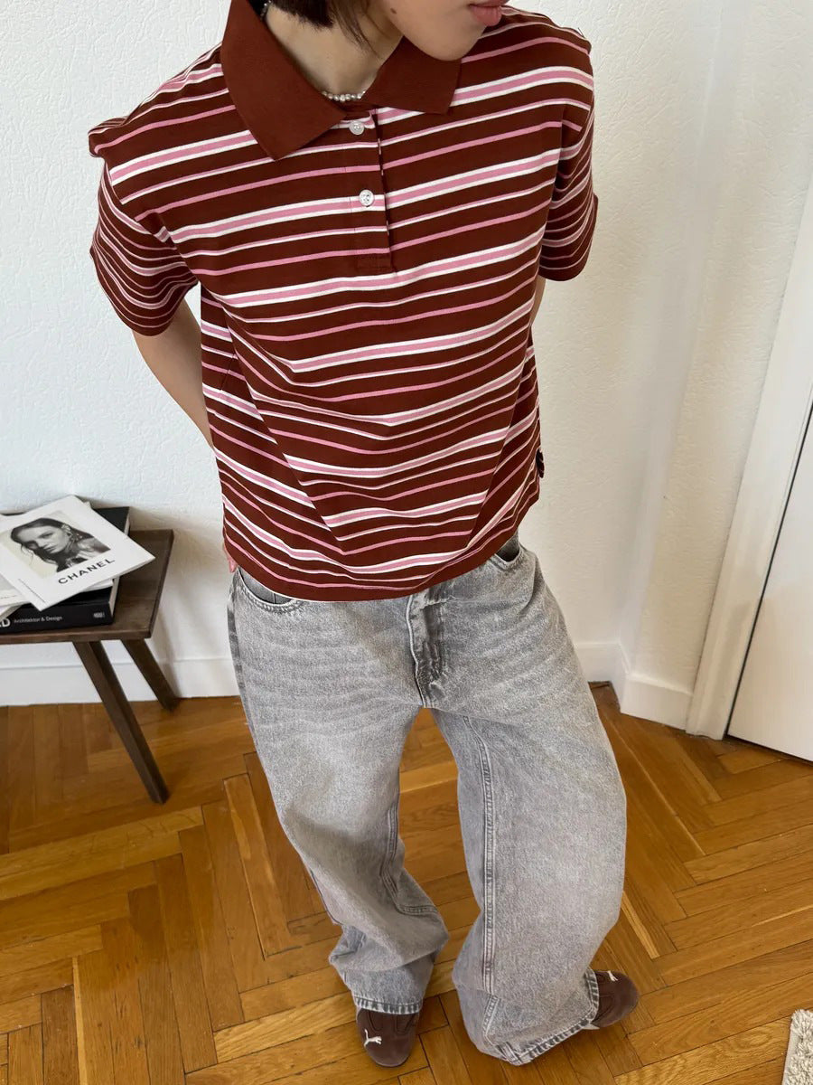 Model stands in brown striped polo shirt with hands behind back, wearing gray denim pants.