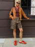 Woman in brown cardigan, red scarf, and loose leopard print shorts, styled with red sneakers and sunglasses.
