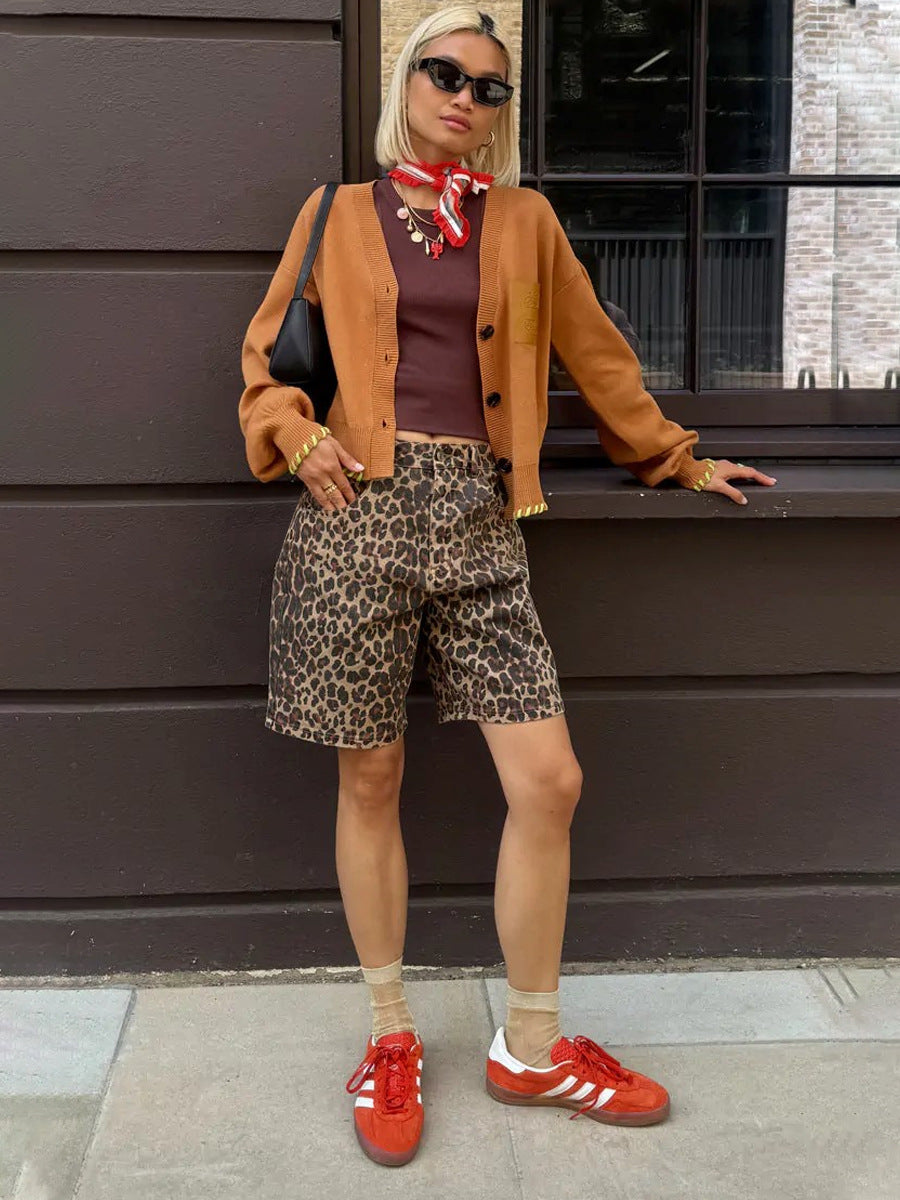 Woman in brown cardigan, red scarf, and loose leopard print shorts, styled with red sneakers and sunglasses.