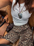 Close-up of woman sitting in a car wearing white tank top and loose leopard print shorts.