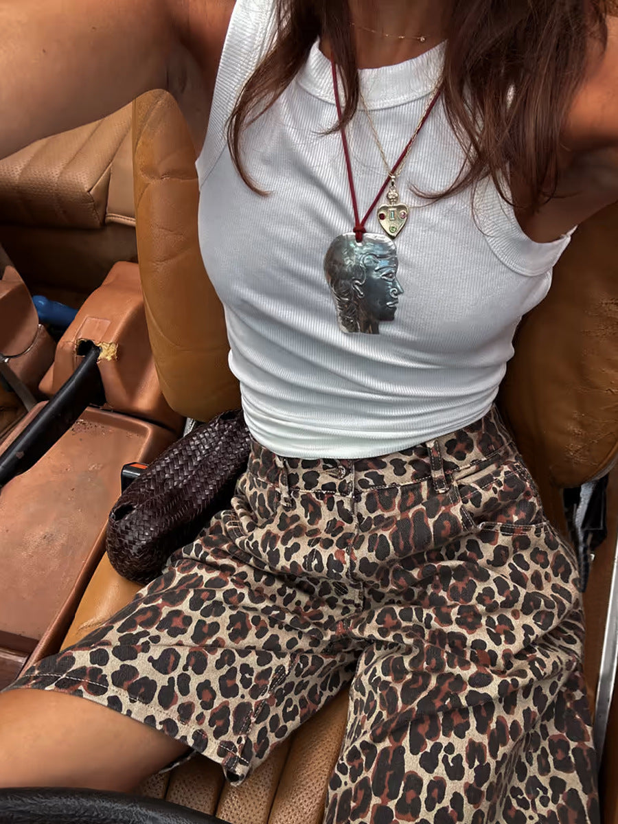 Close-up of woman sitting in a car wearing white tank top and loose leopard print shorts.