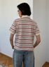 Back view of model in cream and maroon striped polo shirt and loose blue jeans.