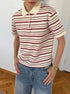Model wears striped polo shirt with short sleeves and spread collar, hands in jeans pockets.