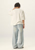 Back view of model wearing an off white heavyweight boxy t shirt showing loose fit and raw bottom hem.
