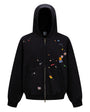 Front product shot of a mens washed black boxy zip up hoodie featuring all-over retro graphic patches on white background.