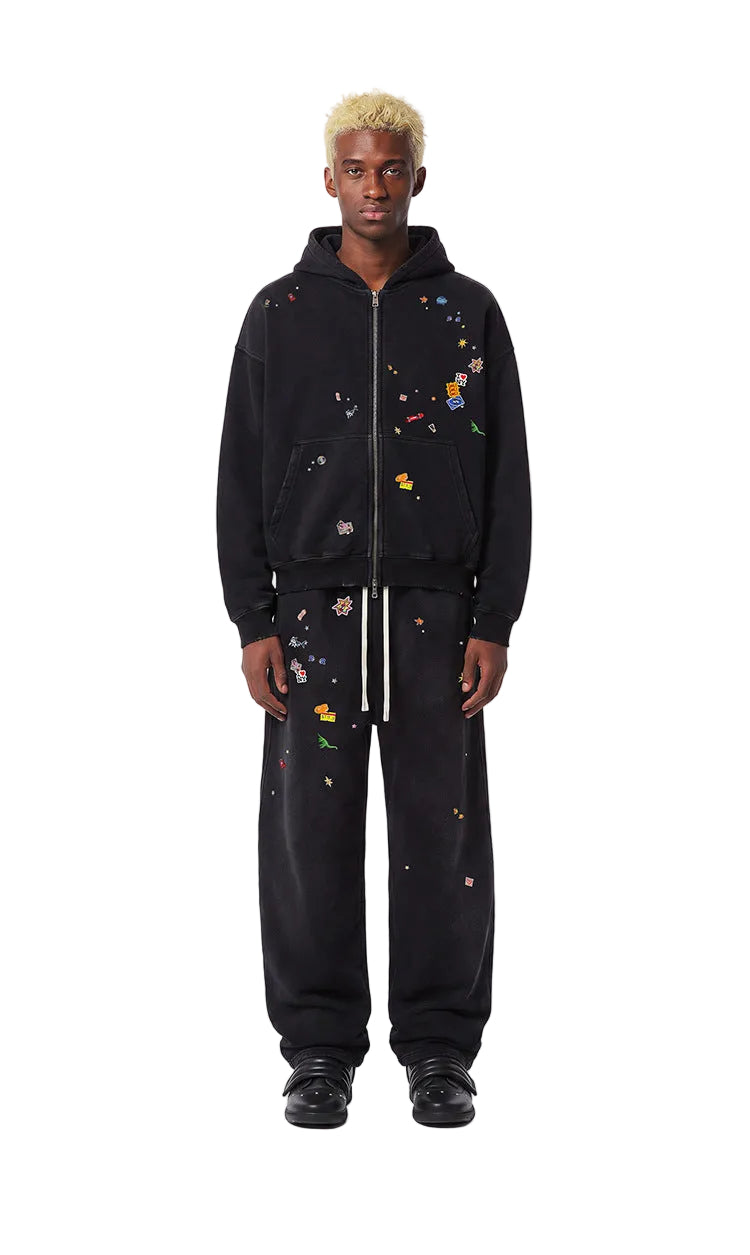 Full length view of model wearing a washed black boxy zip up hoodie with patches and matching sweatpants.