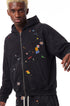 Medium shot of model styling a black boxy fit zip up hoodie with retro graphic patches and drop shoulder sleeves.