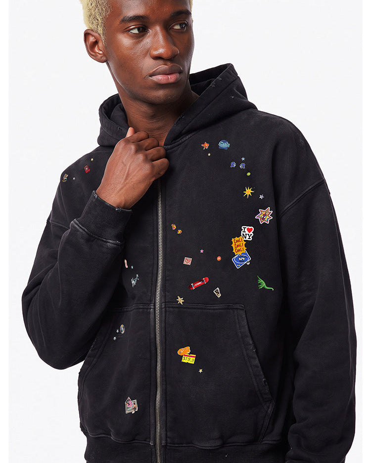 Upper body shot of model wearing a washed black cotton blend full zip hoodie with colorful patch embroidery.