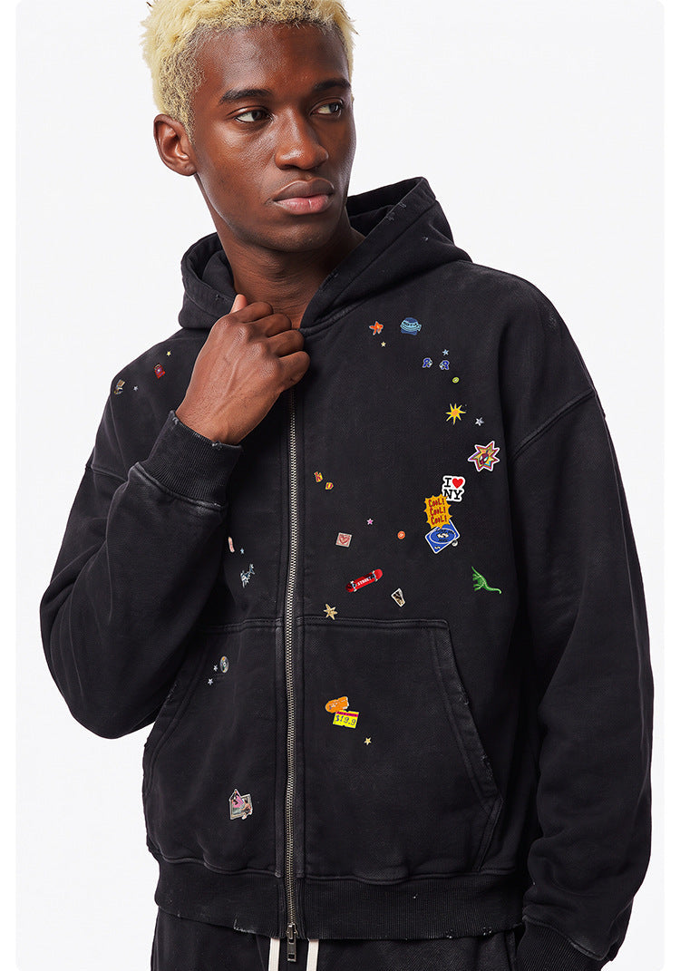 Upper body shot of model wearing a washed black cotton blend full zip hoodie with colorful patch embroidery.